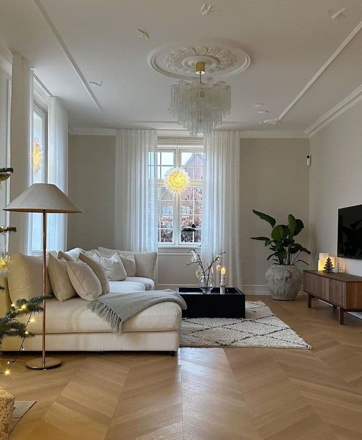 Ljust fiskbensparkett, en takrosett med glaskrona, en krämvit soffa, ett svart soffbord på en berbermatta och en tv-bänk i valnöt, pyntat med juleljus.