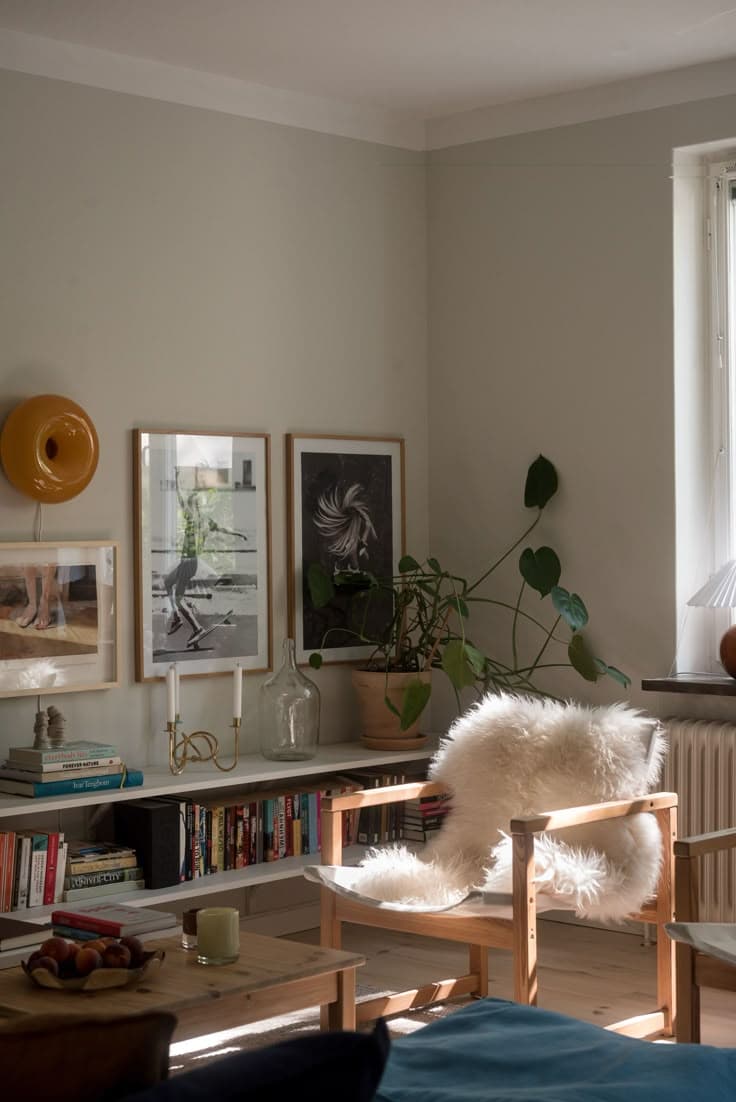 En loungestol i ek med fårskinn, låga vita hyllor fulla med böcker, inramade tryck, en orange vägglampa och en petrolblå soffa ger en levd, samlad hörna.