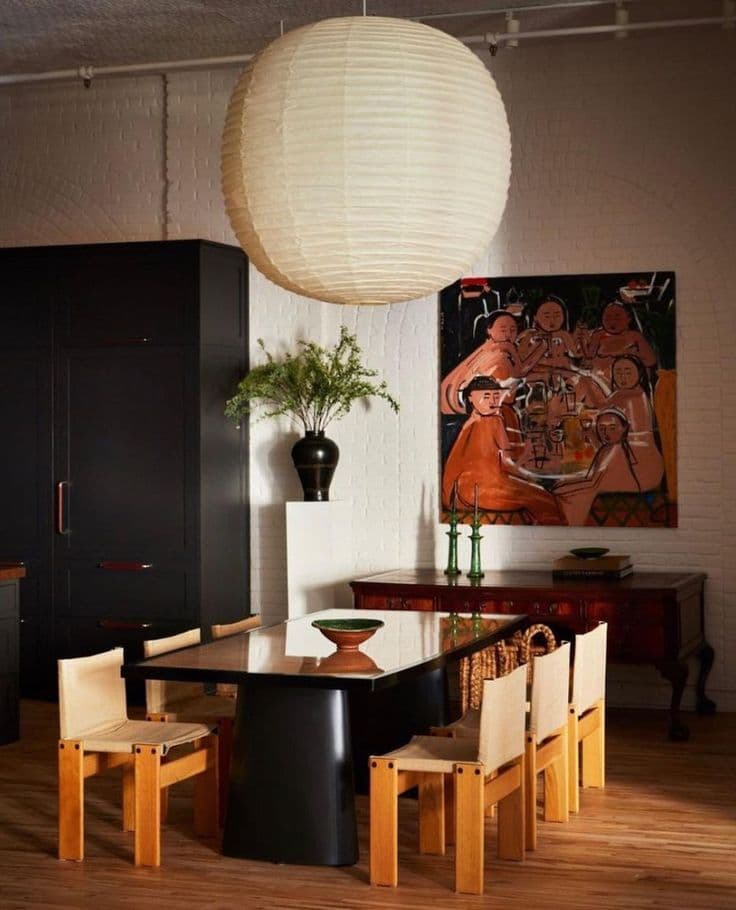 Vitmålat tegel, en jättelik papperslykta, svarta skåp och ett svart matbord med stolar i ljus furu och krämvitt läder bredvid en orange expressionistisk målning.