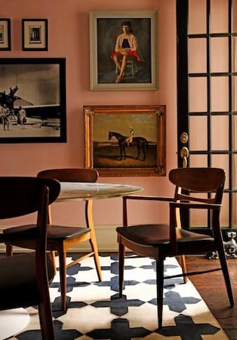 Laxrosa väggar med guldramade porträtt, mittenmodernistiska valnötsstolar kring ett marmorbord och en kraftig svartvit geometrisk matta.