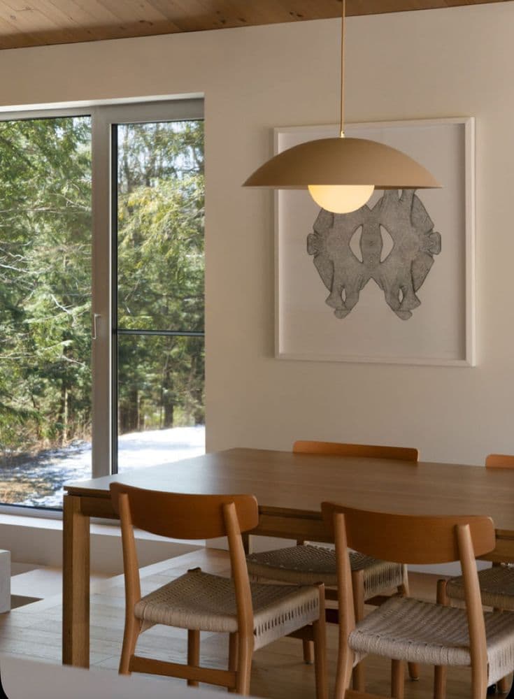 Ett matrum med massivt ekbord, stolar med pappersgarnssits, träklätt tak, en sandfärgad kupolpendel och ett stort fönster mot skogen.
